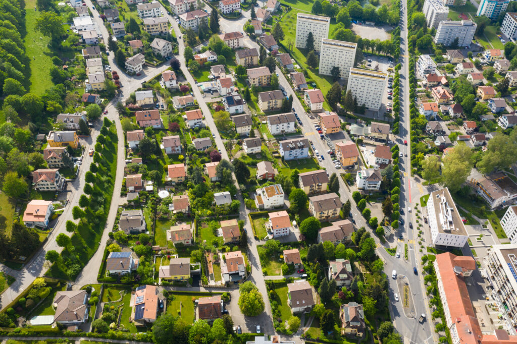 Die Luftaufnahme von Fribourg zeigt eine typische Siedlungsstruktur mit Ein- und Mehrfamilienhäusern sowie kleineren Gewerbebauten.